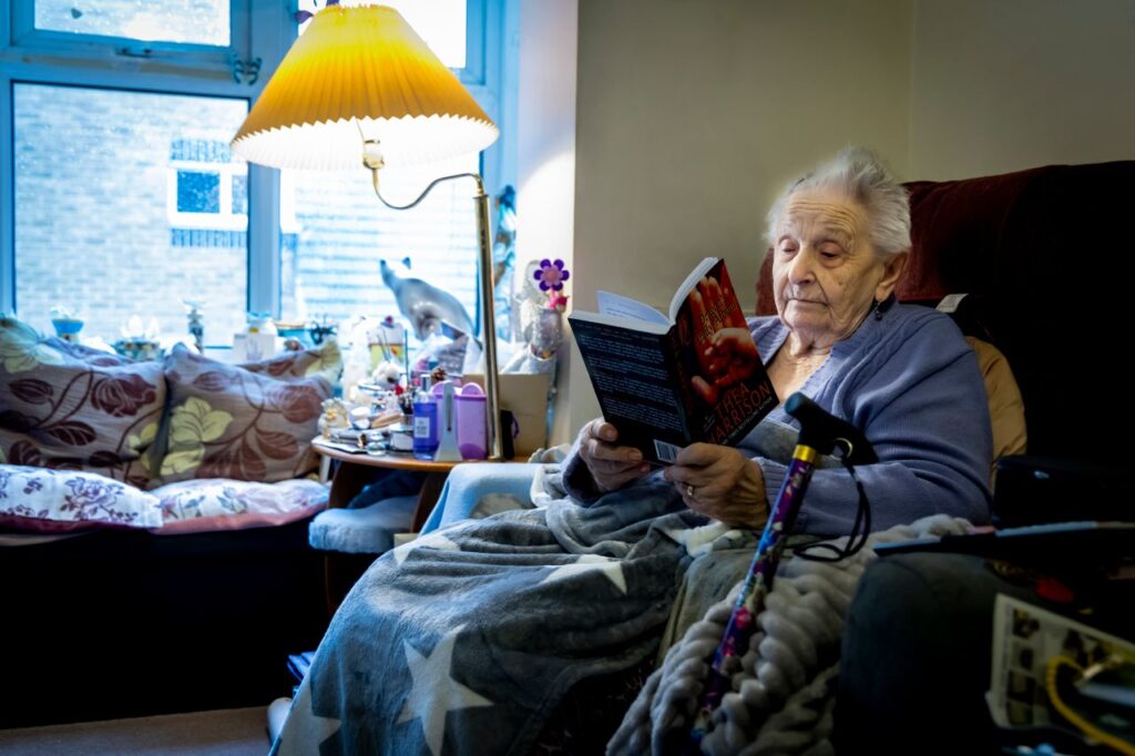 Elderly woman enjoying a book in a cozy living room, embracing retirement leisure time.
